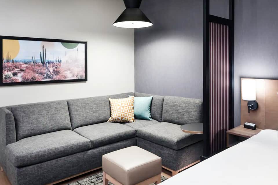 Modern hotel suite with gray sectional sofa, pendant light, desert landscape artwork, and contemporary furnishings
