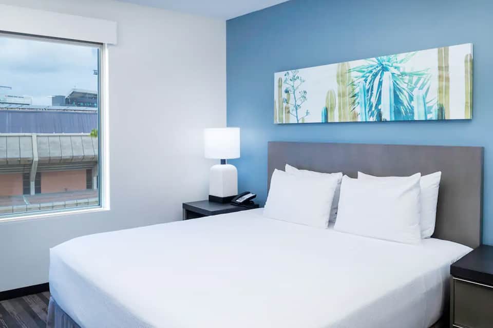 Modern hotel bedroom with queen bed, blue accent wall, ocean view window, and contemporary furnishings