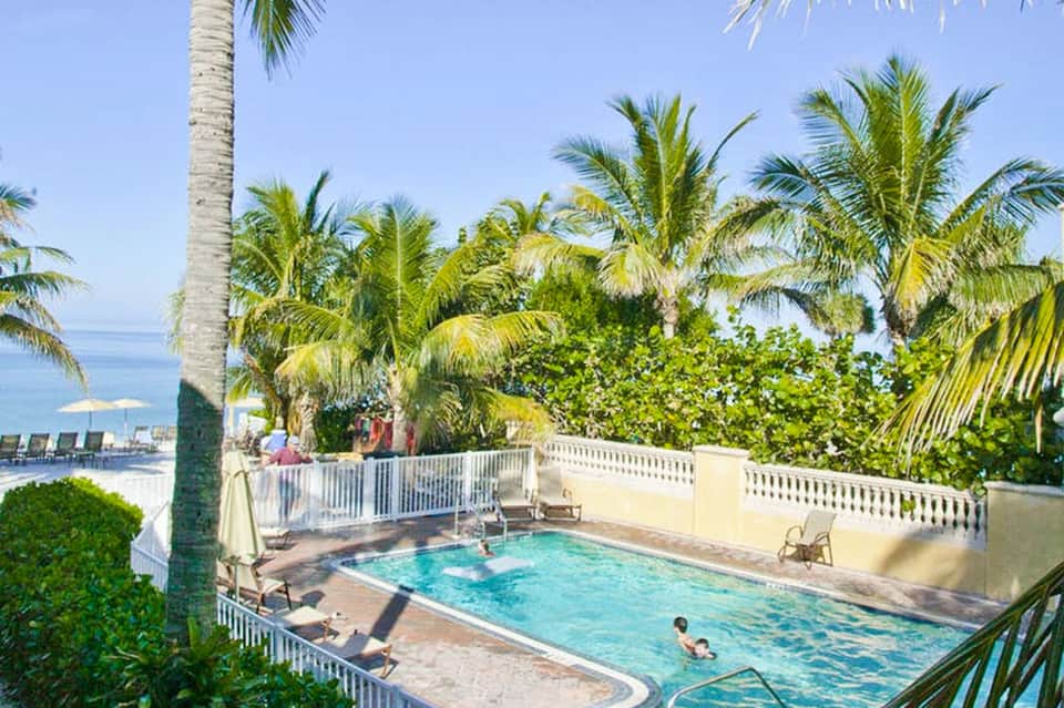Resort pool surrounded by white railings and palm trees with ocean view in background