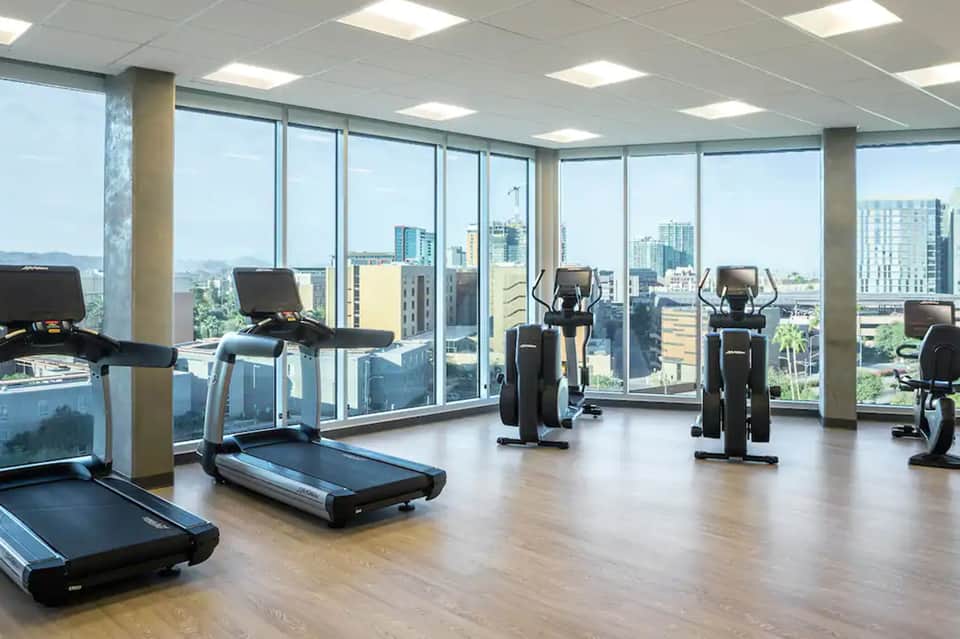 High-rise fitness center with cardio equipment, floor-to-ceiling windows, and city views