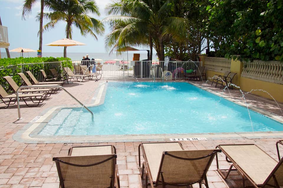 Resort swimming pool with turquoise water, lounge chairs, umbrellas, and palm trees overlooking the beach