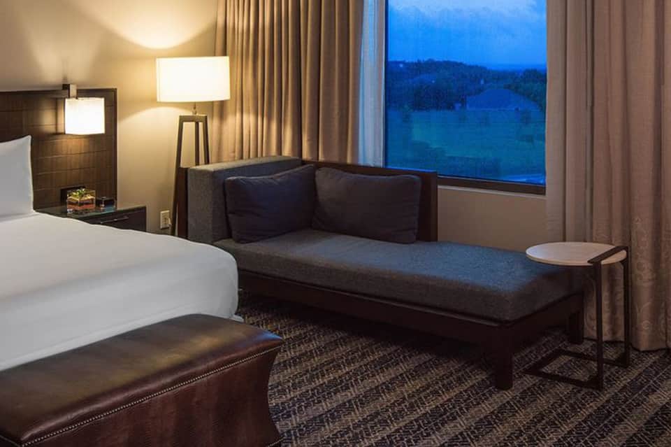 Hotel bedroom at dusk with window overlooking forested lake landscape