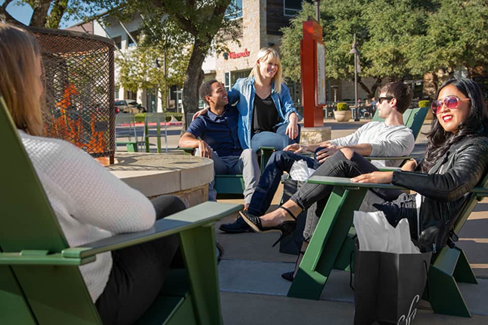 Group of friends socializing on green Adirondack chairs in outdoor plaza setting