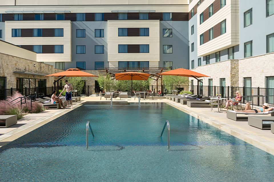 Contemporary resort pool with orange umbrellas, lounge chairs, and residential buildings