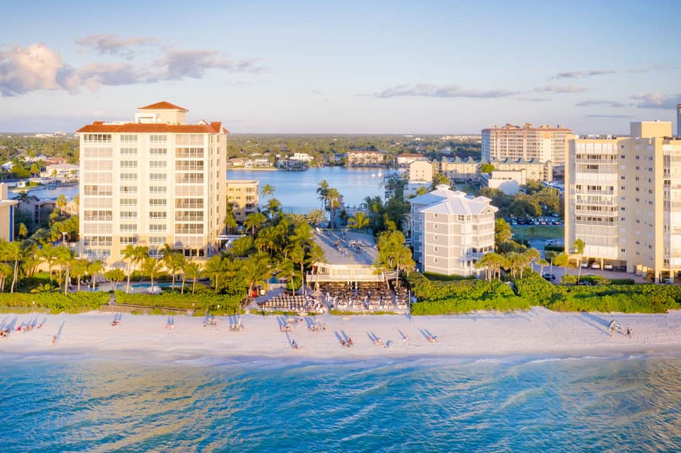 Aerial view of beachfront resort with multi-story buildings, sandy beach, and waterfront pools
