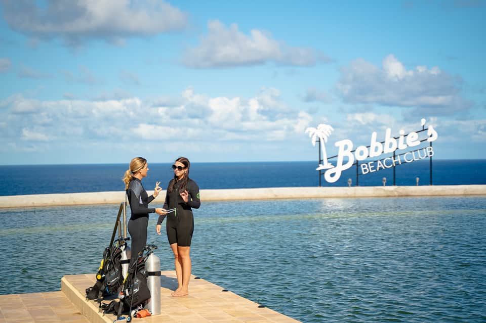 Two scuba divers at beach club dock overlooking ocean