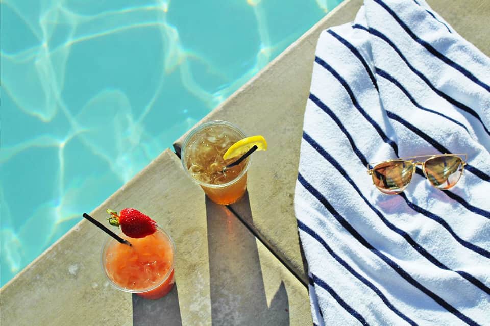 Two cocktails on pool deck beside striped towel and sunglasses with turquoise water