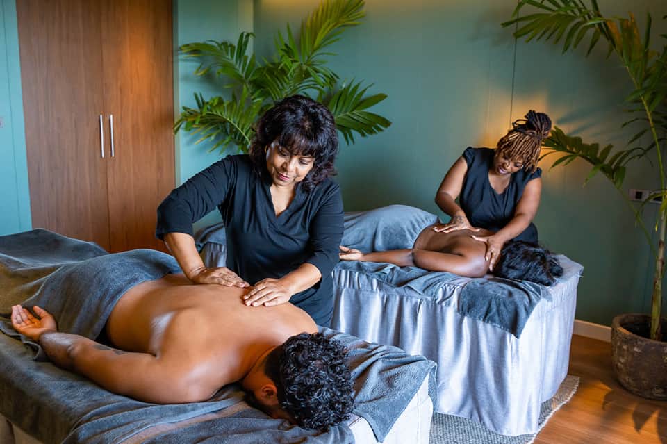 Spa therapists performing massage treatments on clients in calm, plant-filled wellness room