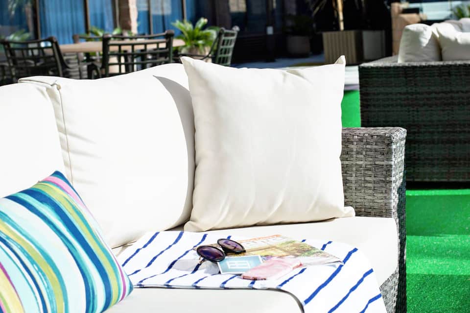 Outdoor lounge seating with white pillows, striped blanket, and colorful cushion on green artificial turf