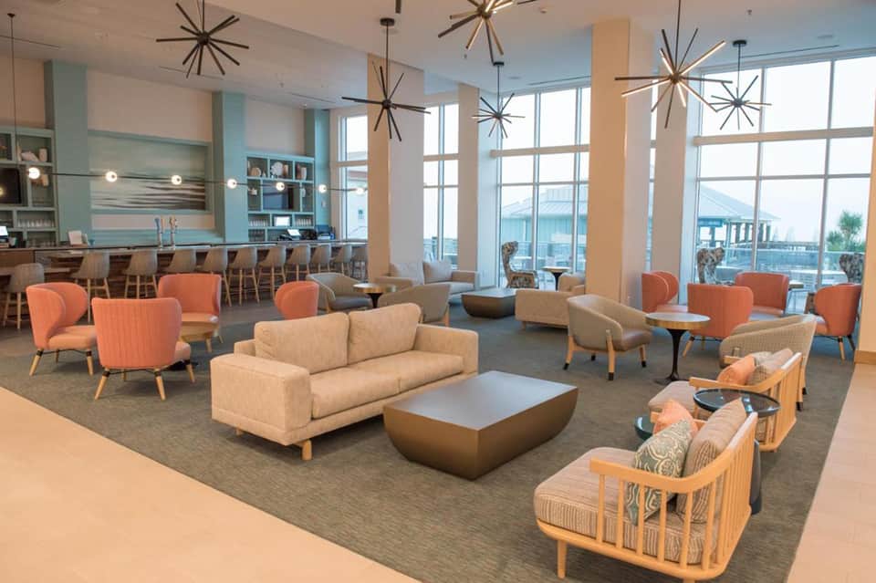 Modern coastal lobby lounge with coral chairs, neutral sofa, starburst lighting, and ocean views
