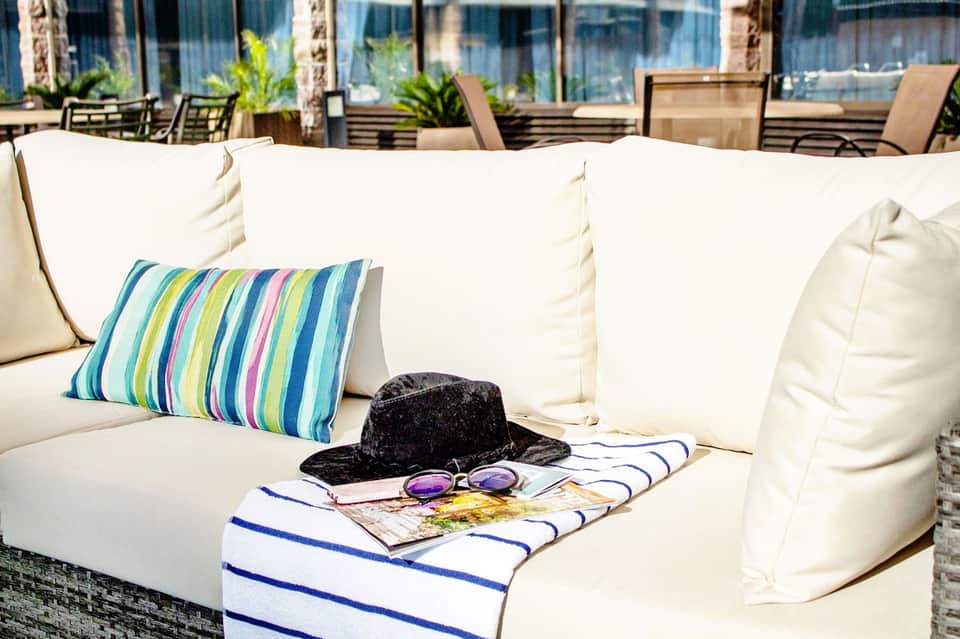 Cream-colored outdoor sofa with colorful striped pillow, hat, sunglasses, and magazine