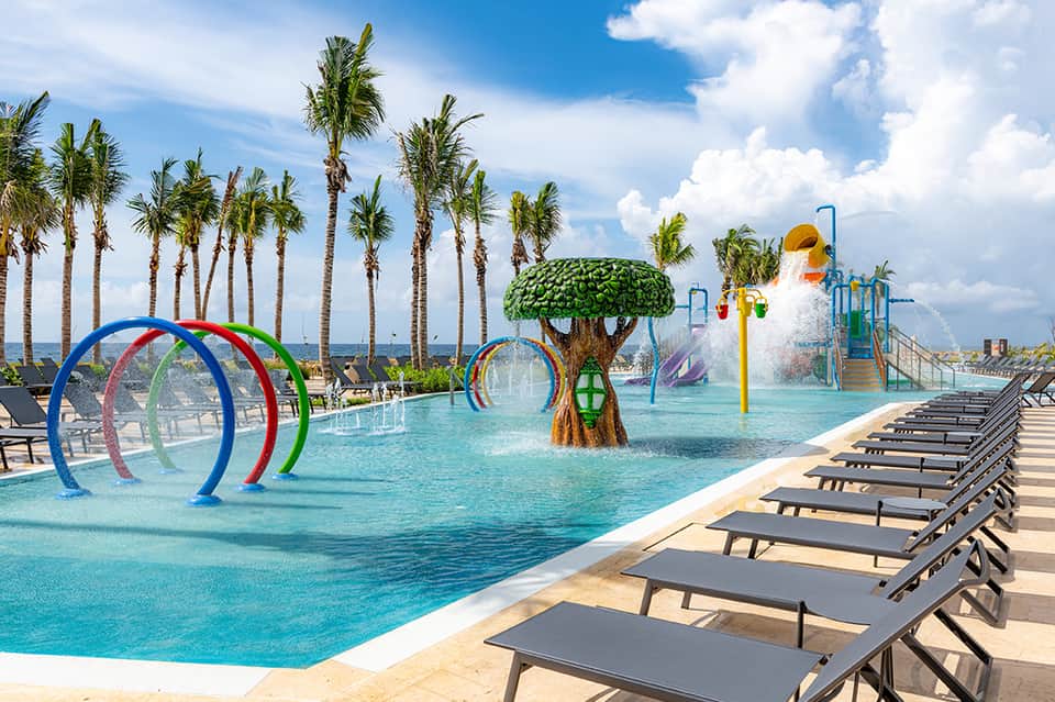 Family water park with colorful splash pad, palm trees, and lounge chairs