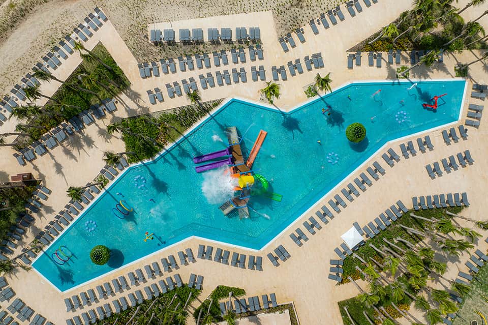 Aerial view of wave-shaped pool with water features, surrounded by lounge chairs and palm trees