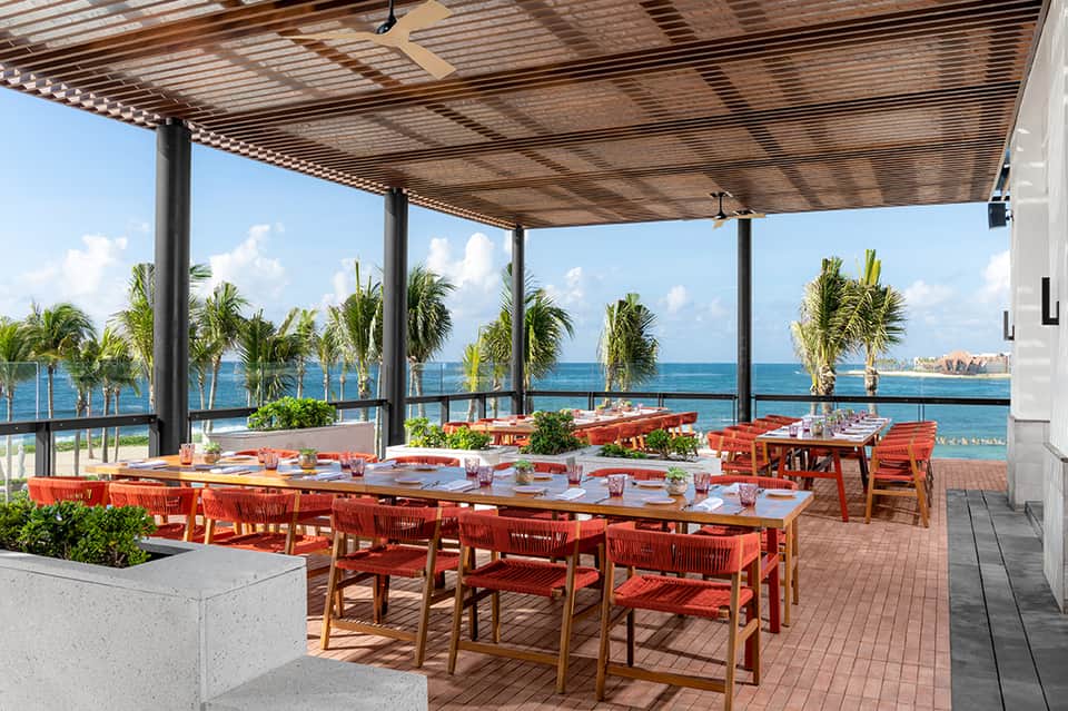 Beachfront dining terrace with red chairs and ocean views through palm trees