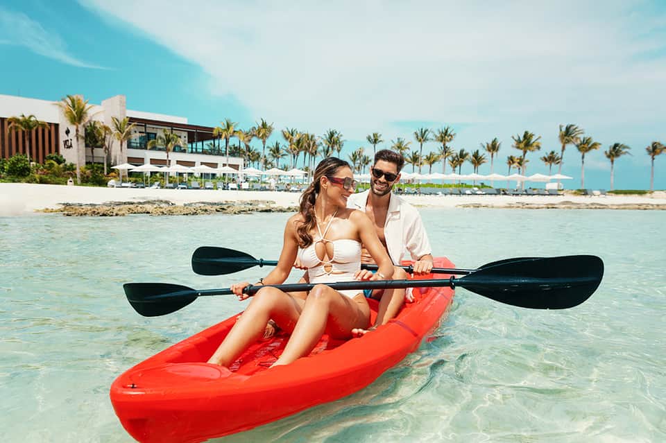 Couple kayaking in turquoise ocean water near tropical beach resort with palm trees