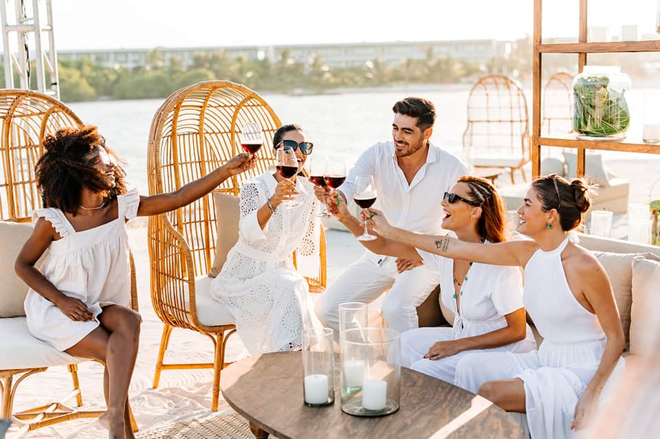 Group toasting with wine glasses at waterfront lounge with orange rattan chairs and river view