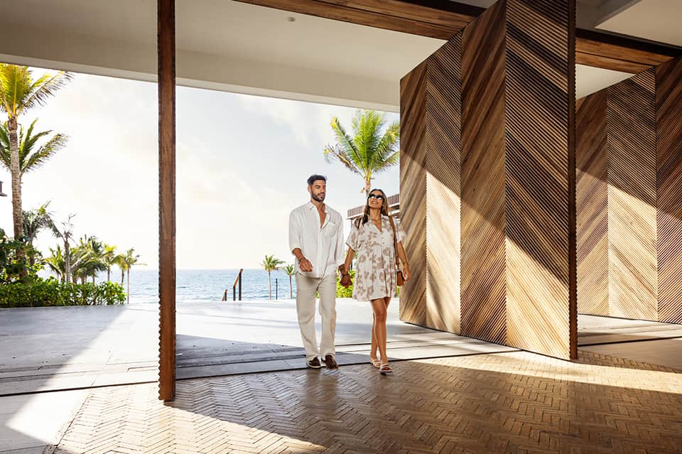 Couple walking through covered breezeway with wooden screens overlooking tropical ocean landscape