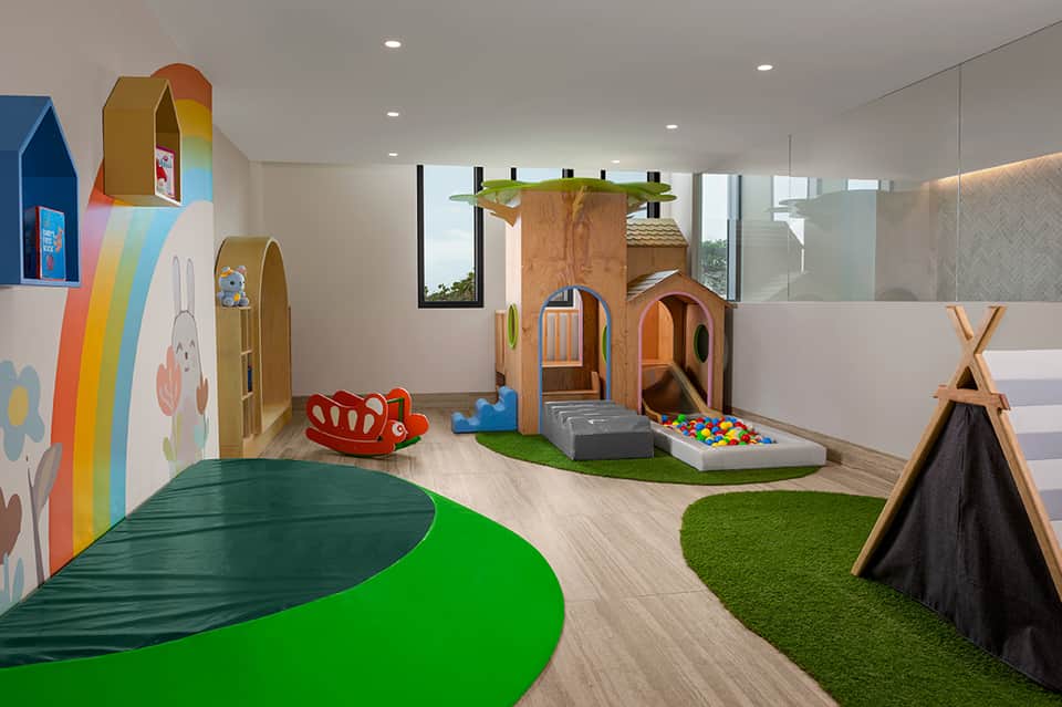 Modern children's play area with wooden play structures, rainbow wall art, and artificial grass flooring