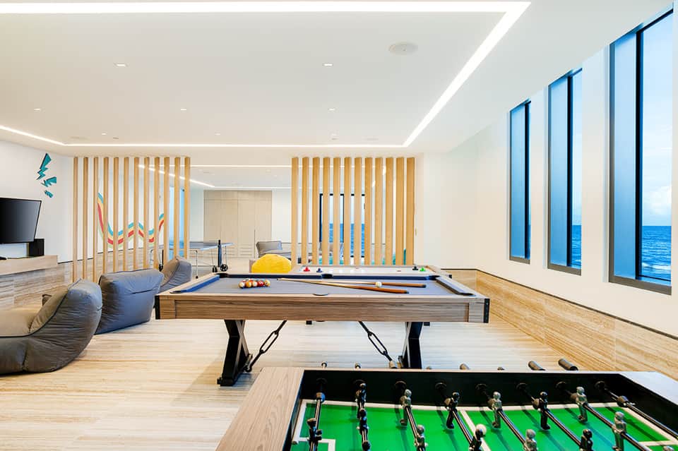 Modern recreation room with pool table, foosball table, and ocean view through large windows