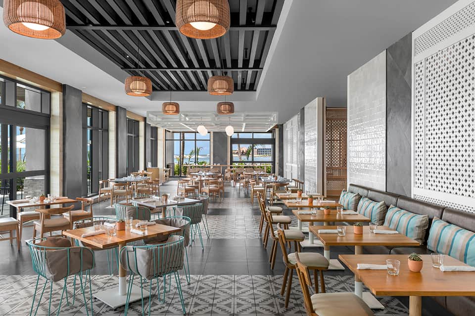 Contemporary dining room with wooden tables, turquoise chairs, pendant lights, and ocean views