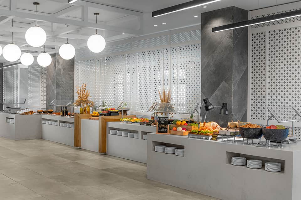 Modern hotel buffet area with white round pendant lights, grey patterned wall panels, and food service stations