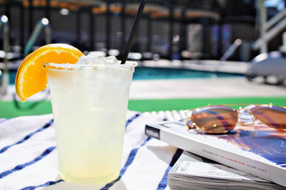 Citrus-garnished cocktail with ice and straw on a poolside table with sunglasses and magazine