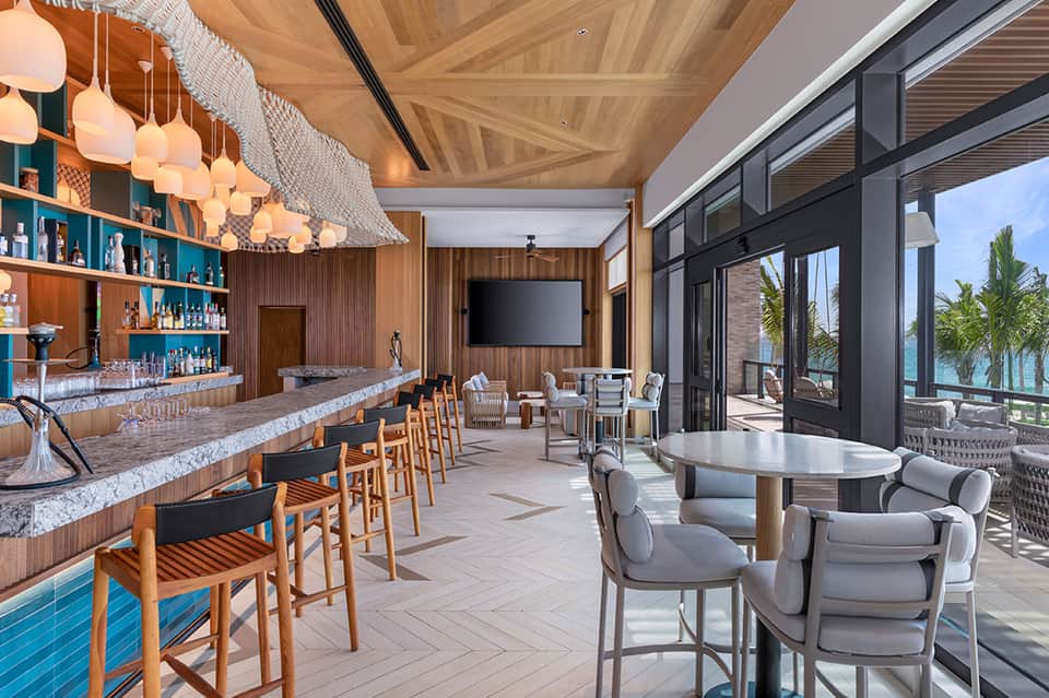 Upscale bar lounge with wooden ceiling, pendant lights, ocean view, and modern seating