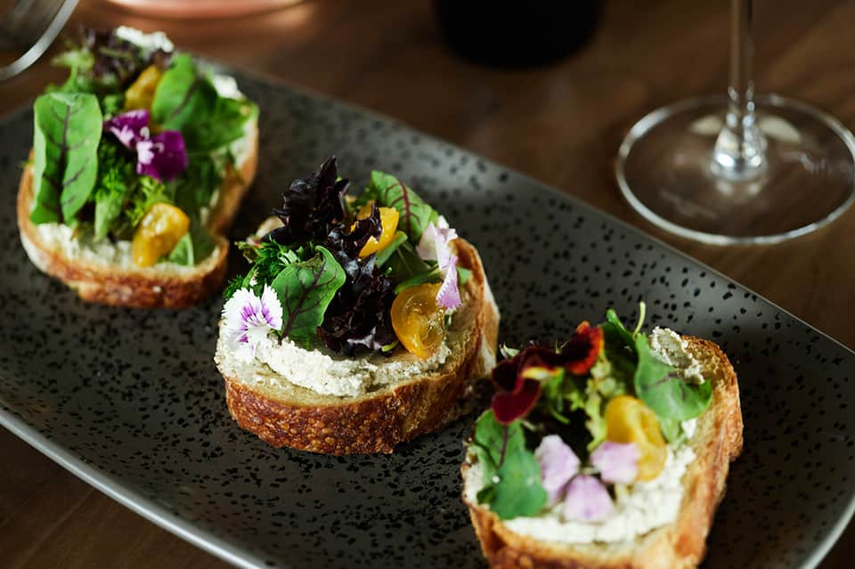 Gourmet appetizers with herbs and edible flowers on dark speckled ceramic plate