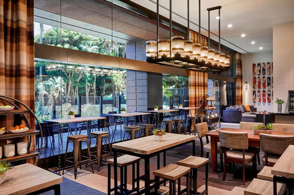 Modern hotel lobby lounge area with wooden furnishings, pendant lighting, and tropical views