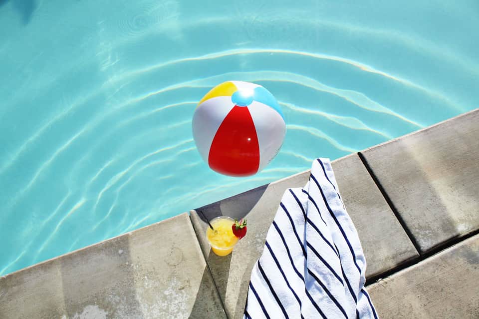 Colorful beach ball floating in crystal clear turquoise pool water with towel on deck