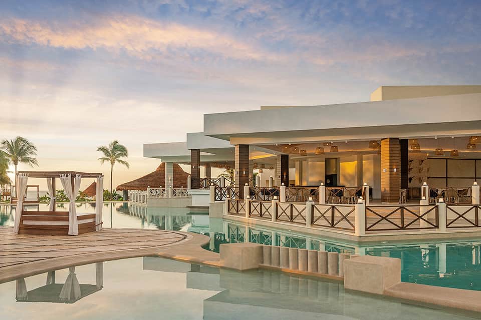Luxury resort infinity pool at sunset with cabanas and palm trees reflected in water