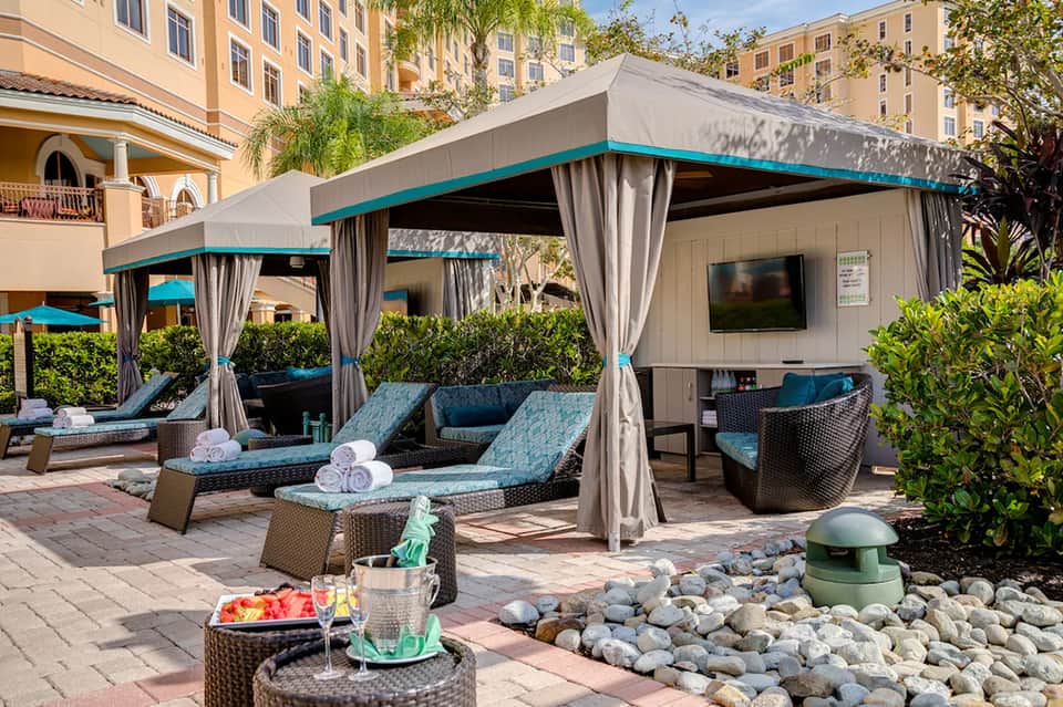 Luxury pool cabanas with turquoise cushions, curtains, and resort buildings