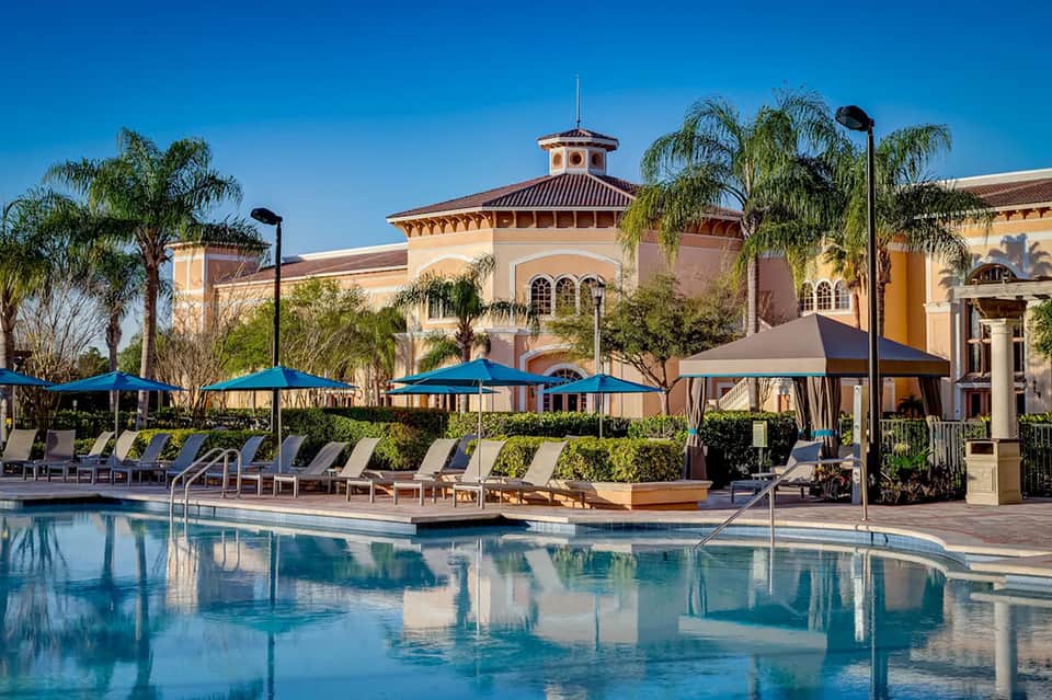 Grand resort pool with blue umbrellas, lounge chairs, and Spanish colonial architecture in sunny daytime