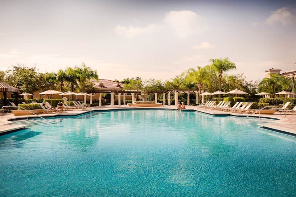Resort zero-edge swimming pool with lounge chairs, white umbrellas, pergolas, and manicured landscaping with palm trees