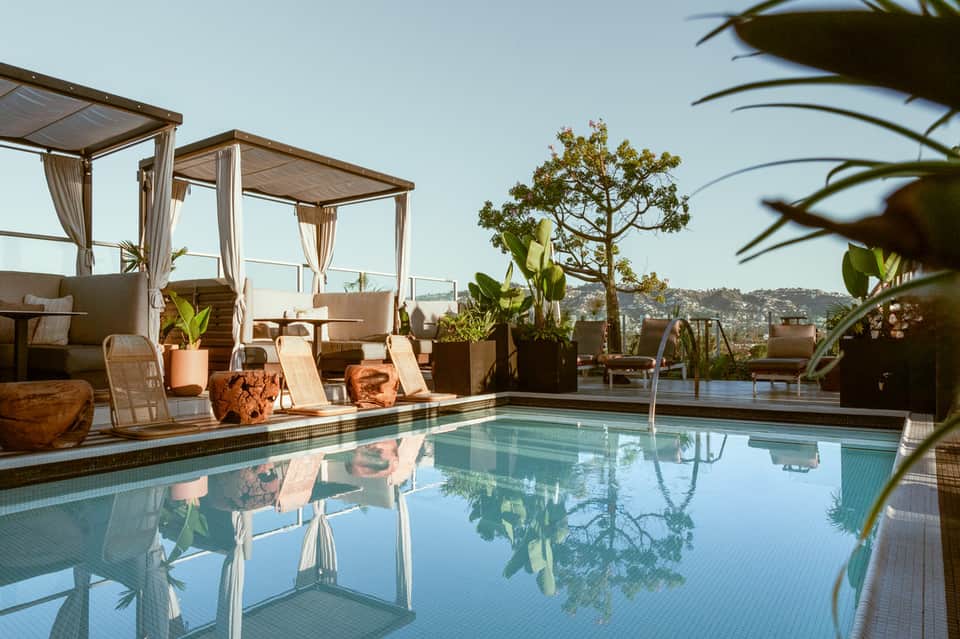 Luxury rooftop pool with cabanas, lounge chairs, and panoramic city views overlooking hillside landscape