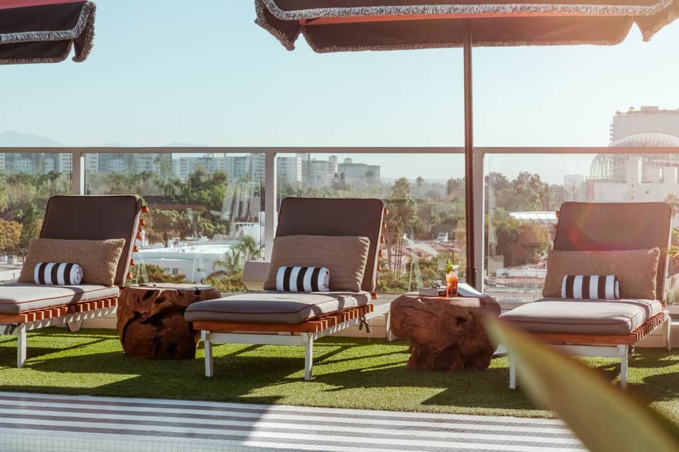 Rooftop lounge with chaise lounges, striped cushions, and city skyline views under brown umbrellas
