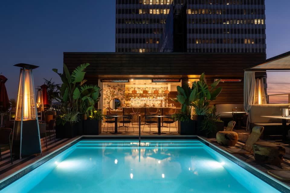 Rooftop pool at night with illuminated bar lounge and city skyscrapers in background