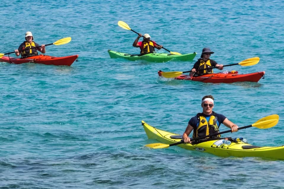 Group of kayakers in colorful kayaks paddling in clear blue ocean water
