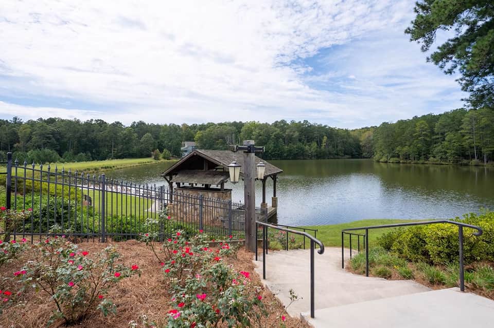 Lakeside gazebo with red flowers, metal railings, and wooden dock structure overlooking calm water