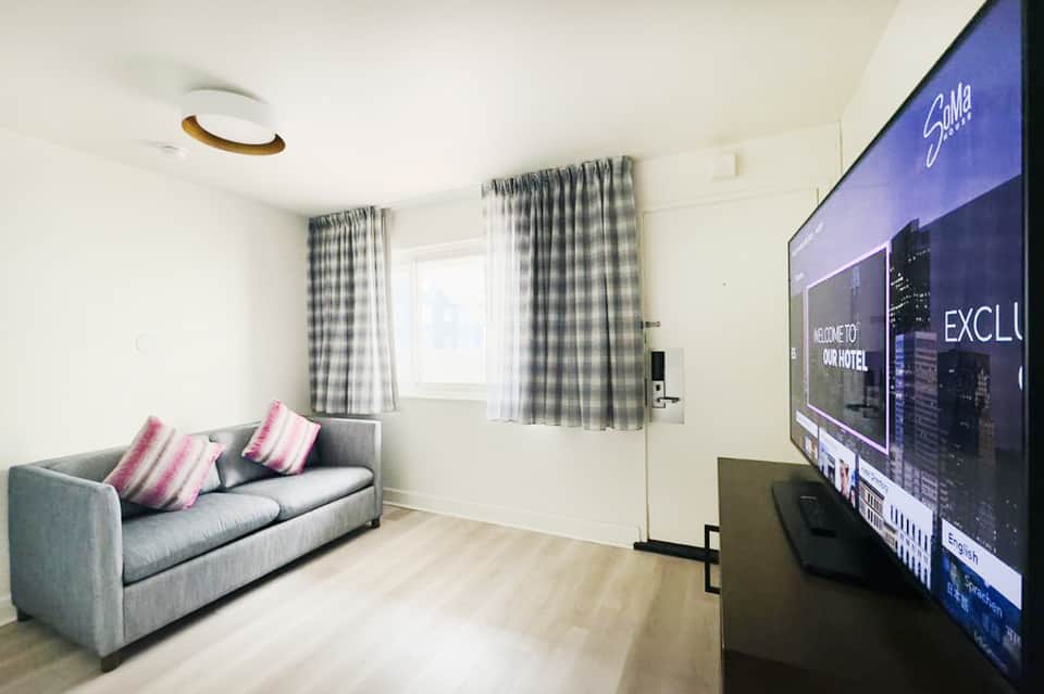 Modern living room with gray sofa, pink striped pillows, checkered curtains, and wall-mounted TV