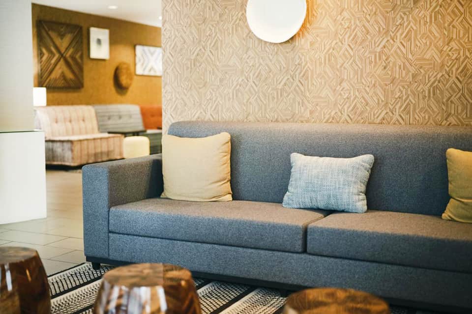 Modern hotel lobby with gray sofa, decorative pillows, patterned wallpaper, and warm lighting fixtures