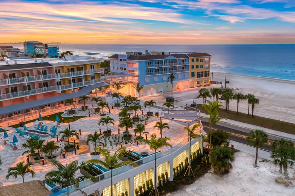 Colorful beachfront resort buildings at sunset with palm trees, pool, and sandy beach