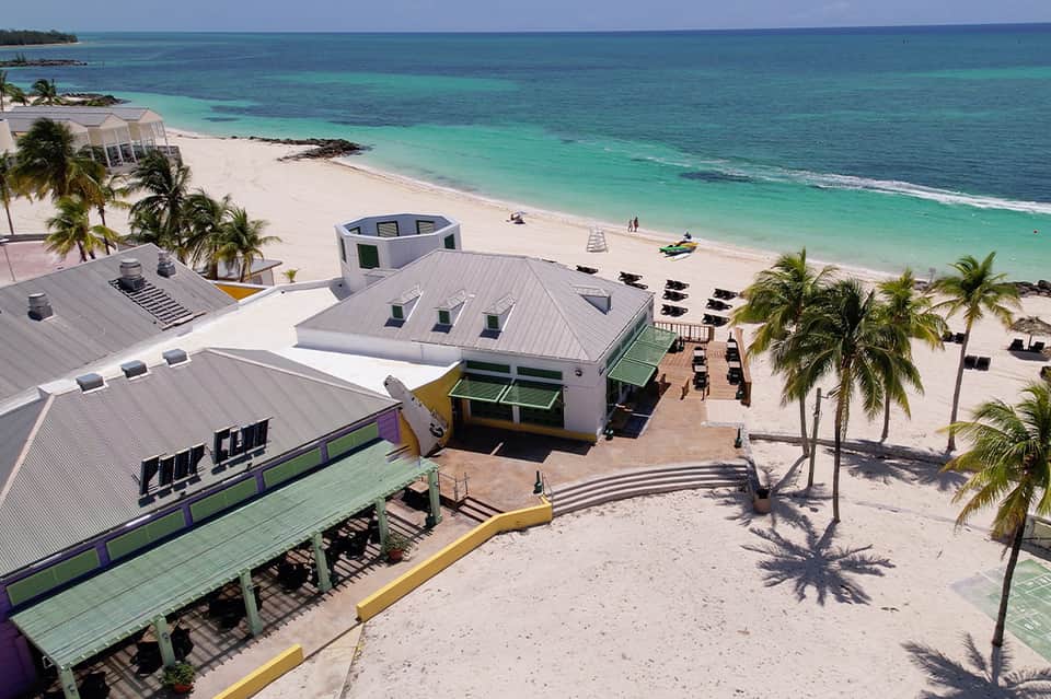 Aerial view of beachfront resort with modern white structures, palm trees, and turquoise ocean waters