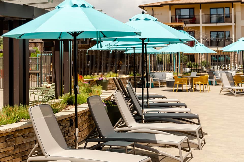 Outdoor pool area with turquoise umbrellas and lounge chairs under stone covered structures