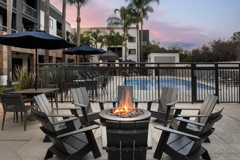 Outdoor firepit lounge with Adirondack chairs, umbrellas, and pool view at dusk