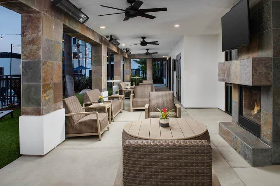 Covered outdoor patio with wicker seating, fireplace, and stone columns overlooking a green lawn