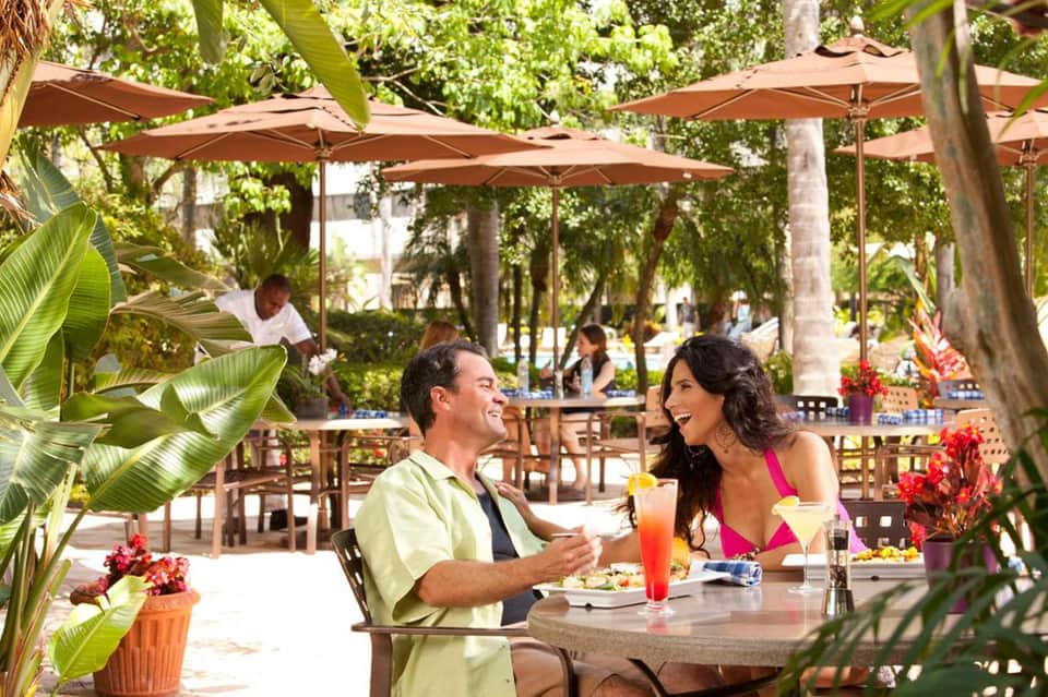 Couple dining outdoors at tropical resort restaurant with umbrellas and lush greenery