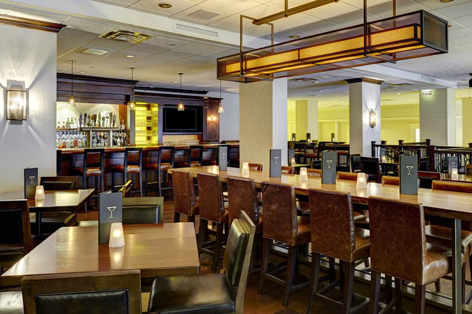 Upscale restaurant and bar with wood accents, pendant lighting, and brown leather chairs at long dining tables