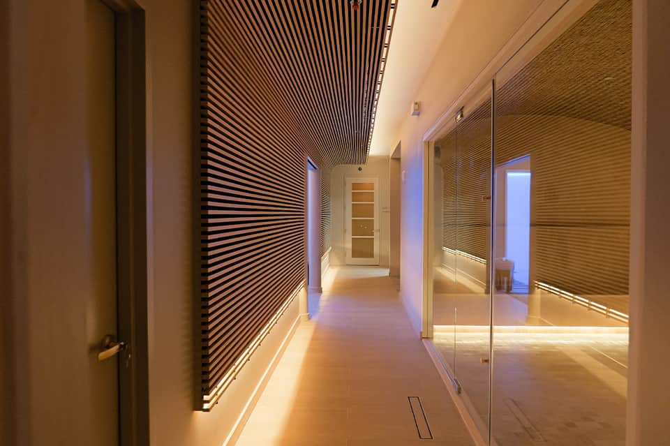 Modern corridor with linear ceiling design, ambient lighting, glass partitions, and minimalist architectural details