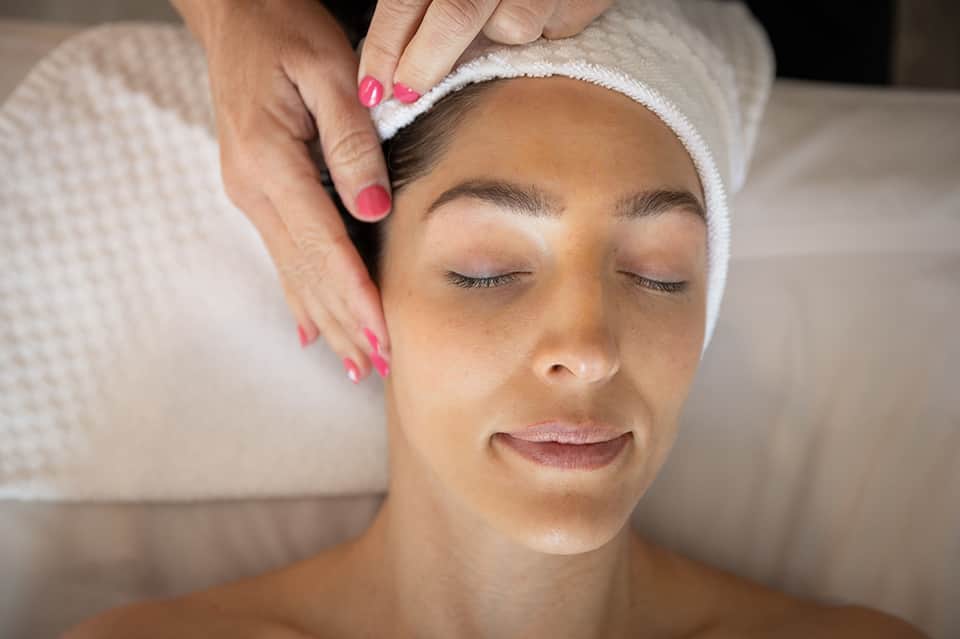 Woman receiving facial massage at spa with headband and closed eyes